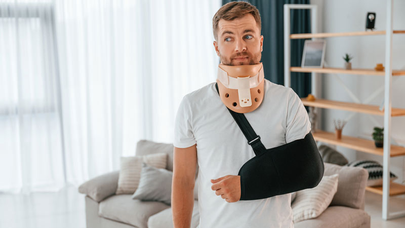 Homem com braço ao peito e colar de pescoço, no interior de uma casa, na sala - alusão a acidentes pessoais